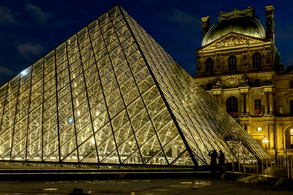 Two tourists take a picture in front of the famous pyramid of the Louvre Museum in Paris