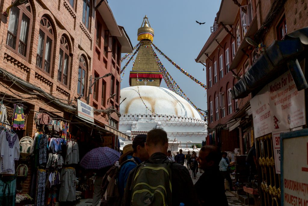 A group of people walk towards the entrance of Boudhanath stupa in Nepal