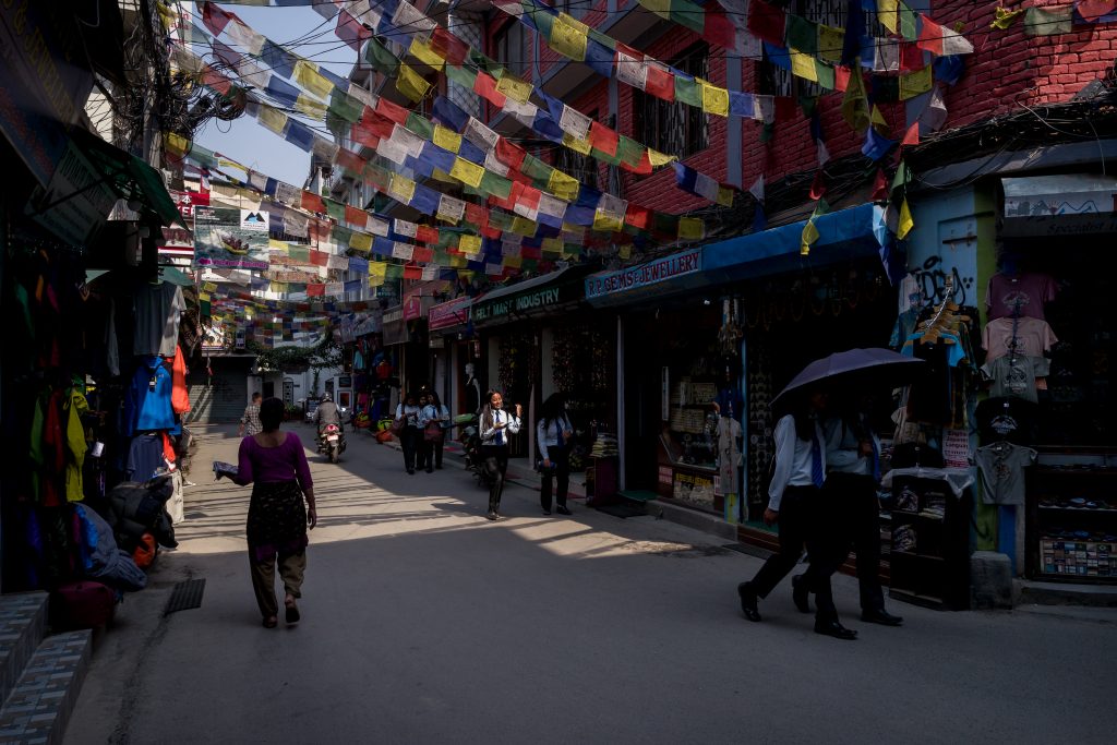 Pedestrians walk through a street lined with Buddhist praying flags in Nepal
