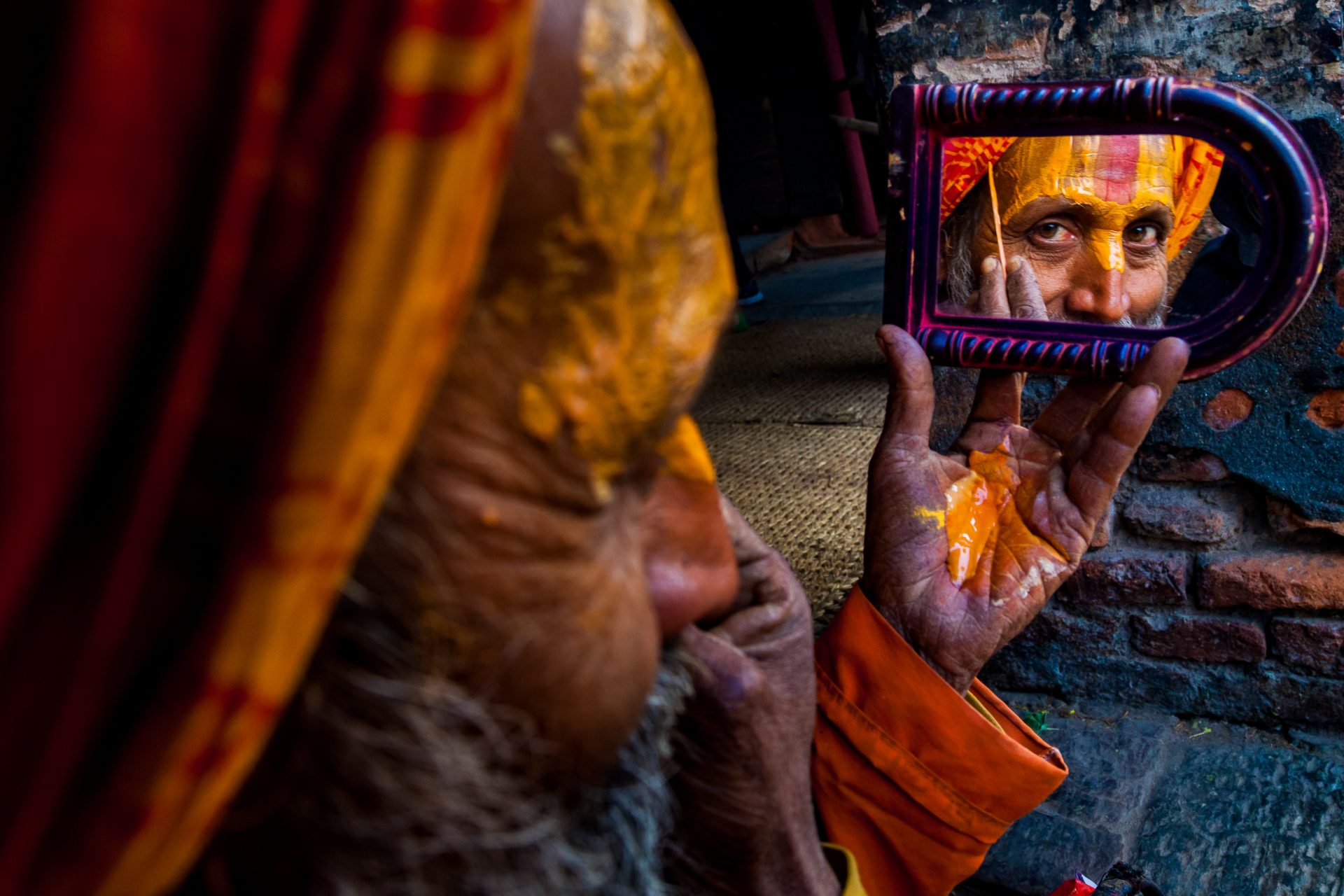 A Shadu, or holy man, looks into a mirror while applying paint to his face in Nepal